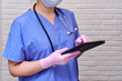 A doctor in a blue uniform presses a finger on the tablet screen. Nursing with a stethoscope with an electronic tablet in hand.