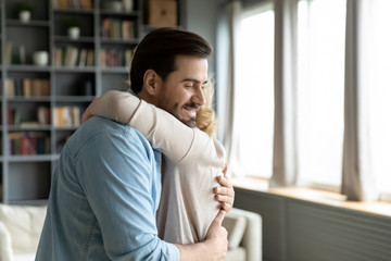 Wall Mural - Caring attentive grown up son visited mother, older mom hugs adult millennial child she missed him enjoy moment, relatives people standing inside of cozy living room feels happy, family bonds concept