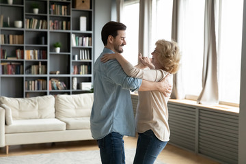 Grown up son came to visit elderly mom, adult child and senior mum standing in living room dancing waltz, people enjoy warm communication having fun indoor, life value, time with aged parents concept