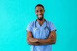 Portrait of a friendly male doctor or nurse wearing blue scrubs uniform and stethoscope, laughing with arms crossed, isolated on blue studio background