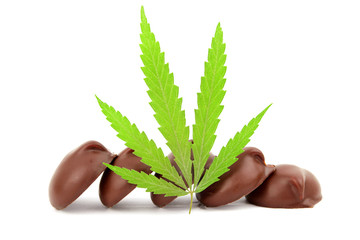 Chocolate sweet candies containing cannabis CBD cannabidiol with a green marijuana leaf on white isolated background. Candy with the addition of medical cannabis CBD or THC