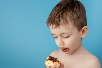 Wall Mural - Little boy eating donut chocolate on blue background. Cute happy boy smeared with chocolate around his mouth. Child concept, tasty food for kids