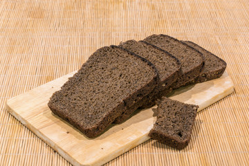 Slices of black bread lie on a cutting board on a bamboo napkin