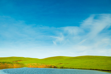 Wall Mural - Green meadow with lake and hills and cloudy sky