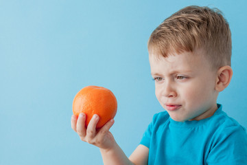 Wall Mural - Little Boy Holding an Orange in his hands on blue background, diet and exercise for good health concept