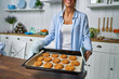 .Young beautiful housewife holding freshly baked cookies on a tray in the kitchen