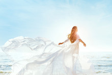 Woman On Sunny Sea Beach In White Fluttering Dress, Fashion Model Back Rear View, Silk Cloth Waving On Wind