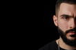 close-up of a dramatic portrait of a young serious guy, a musician, singer, rapper with a beard in black clothes . half a face on a black isolated background.
