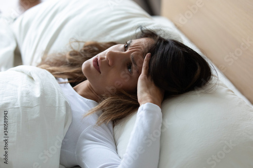 Close up unhappy woman suffering from insomnia or headache, touching head, sleepless tired girl with open eyes lying in bed under warm blanket, feeling unwell, lack of sleep, early morning awakening