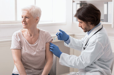 Doctor injecting vaccine to senior woman at clinic