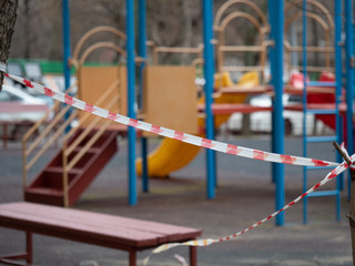 Closed empty playground.  Red and white barrier tape in focus. Quarantine. COVID-19