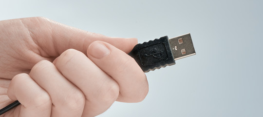 Wall Mural - Hand holding black USB cable isolated on gray background.