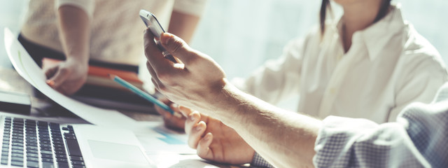 Fototapete - Group of young business people working together. Loft office and smart casual dress code. Researching new product strategy. Electronic devices and paperwork on the table. Wide screen panoramic