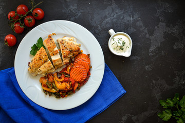 Wall Mural - Baked chicken breast with vegetables. Chicken breast, asparagus, carrots, in a white plate. Top view. Dark background. Free space for text. Blue linen napkin.