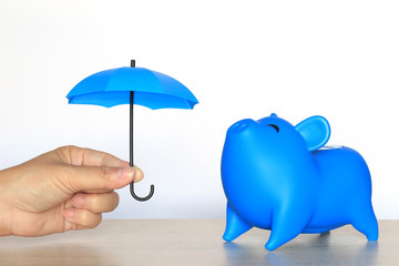 Protection, Blue piggy bank with hand holding the blue umbrella on white background, Finance insurance and Safe investment concept