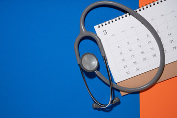 Wall Mural - Top view of stethoscope and calendar on the blue and orange background, schedule to check up healthy concept