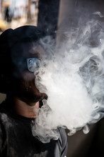 Vertical Photo Of A Black Young Man With Sunglasses And A Vintage Hat Pulling Smoke Out