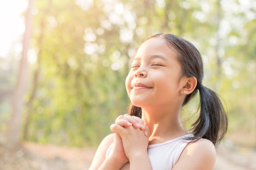 Wall Mural - cute little girl hands praying to god with the bible in the morning on nature background.  little asian girl hand praying for thank god. copy space. spirituality and religion faith hope concept.