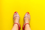 Fototapeta  - female legs and summer open toes shoes on colorful background. Yellow background, free copy space. Overhead shot of elegant shoes of pastel color. Top view