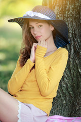 Wall Mural - Jeune femme avec un chapeau de paille bleu souriante au pied d'un arbre