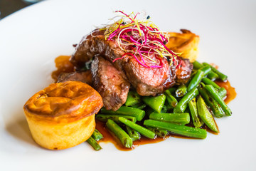 Medium rare beef steak and green vegetables on a white plate.Beef steak and vegetables on a white plate