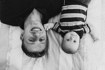 Young dad and baby are lying in bed and smiling. Black and white photo of a young dad and baby.