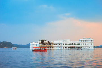 Fototapete - Romantic luxury India travel tourism - tourist boat in front of Lake Palace (Jag Niwas) complex on Lake Pichola on sunset with dramatic sky, Udaipur, Rajasthan, India