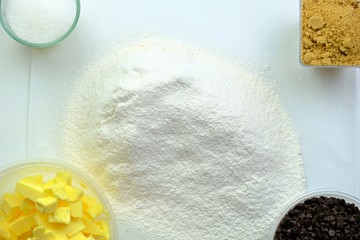 Ingredients for homemade bakery consisting of white sugar, soft brown sugar, unsalted pure butter slice, chocolate chips and organic self-rising flour.