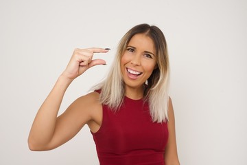 Blonde European woman over isolated background gesturing with hand showing small size, measure symbol. Smiling looking at the camera. Measuring concept.