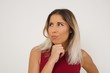 © Jihan - Isolated portrait of stylish young European woman with hand under chin and looking sideways with doubtful and skeptical expression, suspect and doubt. Standing indoors over background.