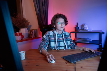 Young freelancer working from home sitting in a cosy chair at the desk with computer.