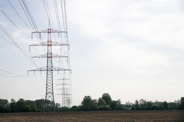 high voltage power lines, red and white electricity pylon with blue sky and green field with trees, symbol for infrastructure, energy and nature