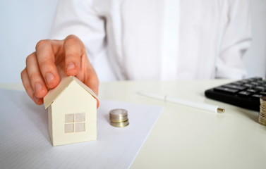 Saving to buy a house, which the hand puts money in, the coins stack is growing, saving money. Paper house and female hand, calculator on a white table