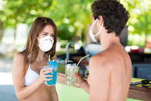 Young Masked People Talking In A Beach Bar, Funny Coronavirus Pandemic Concept In Summer
