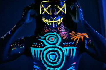 handsome african guy in mask with fluorescent body art, unrecognizable shirtless man posing, fashion model with colorful prints on skin