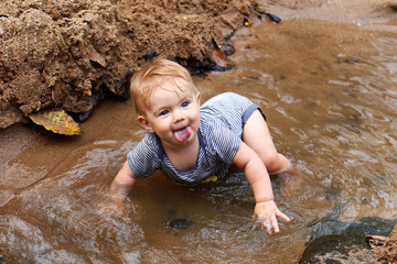 Little cheerful girl with blond hair in sundress is playing in mountain river.