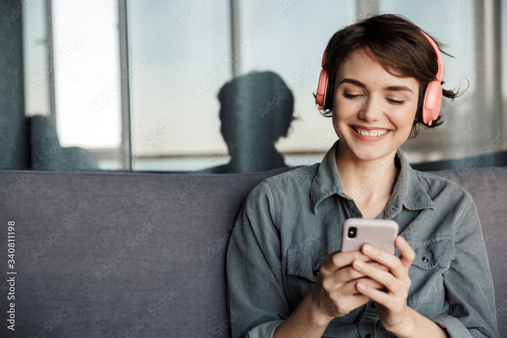 Image of nice young smiling woman using smartphone and headphones - obrazy, fototapety, plakaty 