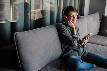 Wall Mural - Image of nice young smiling woman using smartphone and headphones