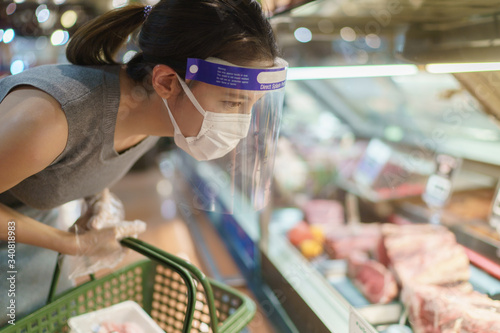 Fotografía Woman wearing gloves, face shield and mask choosing meat at supermarket