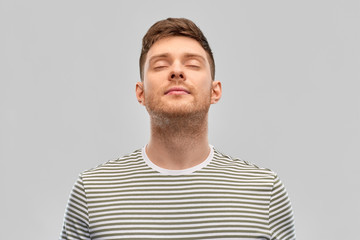 wellness and people concept - happy young man in striped t-shirt breathing over grey background