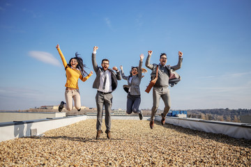 four excited happy business people jumping on rooftop and cheering for success.