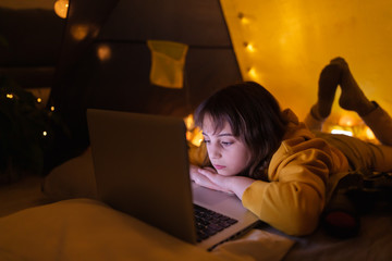 Wall Mural - little 11 year old girl using laptop under her home-made tent inside the living room.