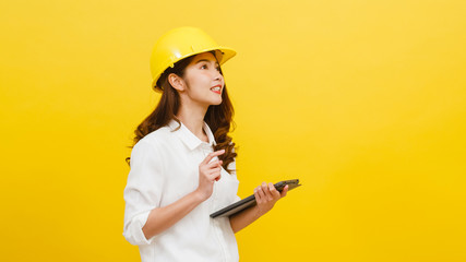 Young Asian woman engineer using digital tablet with positive expression, dressed in casual clothing and looking at camera over yellow background. Happy adorable glad woman rejoices success.