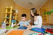 © Andrii - A young mother is doing homework with her son at home. Parents and training