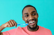 © Carlos David - Portrait of a happy young man in pink shirt and great smile brushing teeth with toothbrush and looking to side, isolated on blue