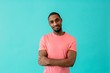 © Carlos David - Portrait of a young man smiling with arms crossed, against blue studio background