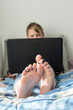 © Ruslan - Bare feet, distance learning during quarantine, a boy sitting on a sofa with a laptop, home schooling.