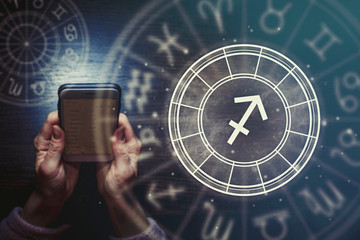 Wall Mural - female hands are holding a phone and an astrological circle with the zodiac sign sagittarius against