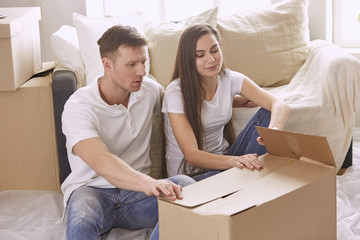 Portrait of happy couple looking at laptop computer together sitting in new house, surrounded with boxes