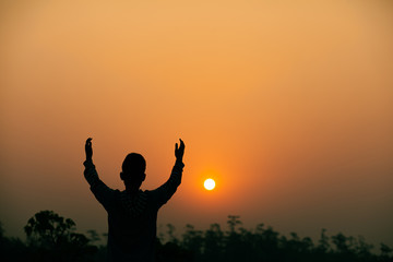 Wall Mural - Boy lift hands up and praying to God on sky with light sunset background, Christians should worship and thank God, christian silhouette concept.